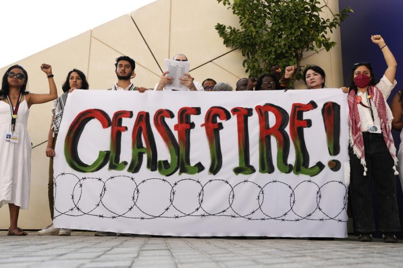 Demonstran mengangkat tinju mereka dan tanda yang menyerukan gencatan senjata dalam perang Israel-Hamas di KTT Iklim PBB COP28, Ahad, 3 Desember 2023, di Dubai, Uni Emirat Arab. 