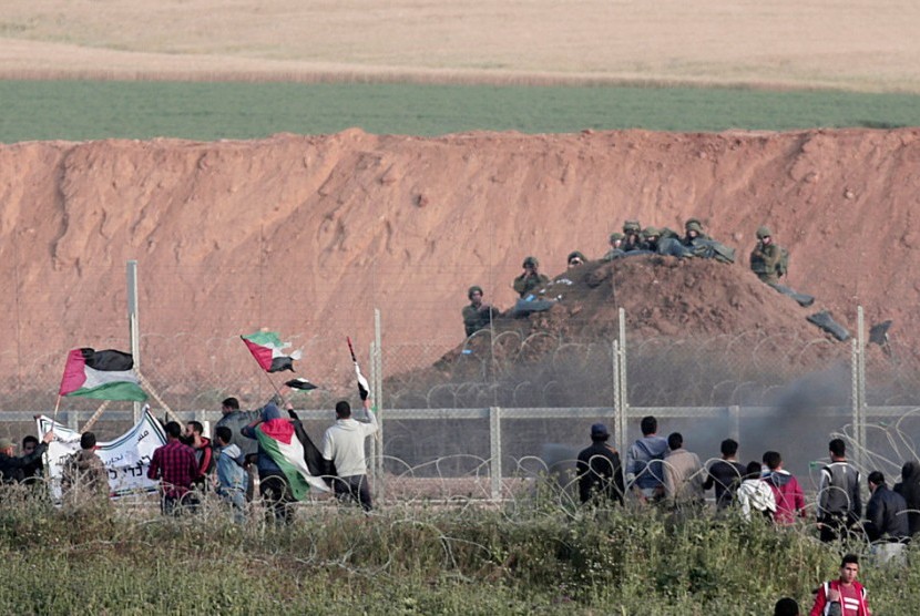 Demonstran Palestina melambaikan bendera di hadapan tentara Israel.