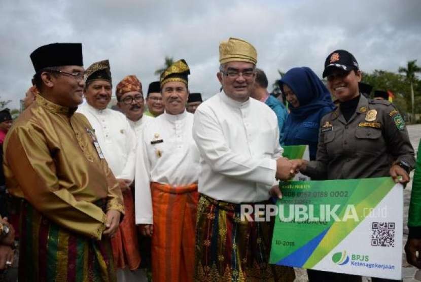 Direktur Investasi BPJS Ketenagakerjaan Amran Nasution menyerahkan katru kepada para perwakilan pekerja rentan penerima BPJS ketenagakerjaan disaksikan Bupati Siak Syamsuar (tengah) dan Direktur Utama Bank Riau Kepri Irvandi Gustari (kiri) di kantor Bupati Siak, Riau, Jumat (12/10)