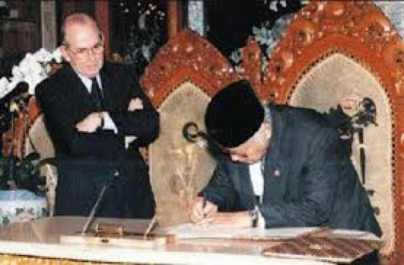 Direktur Pelaksana IMF, Michel Camdessus  dengan bersedekap memperhatikan Presiden Soeharto yang tengah menandatangi perjanjian dengan IMF pada 1998.