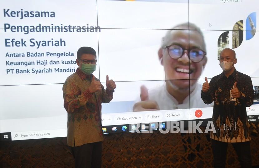Direktur Utama Mandiri Syariah Toni EB Subari (kiri) didampingi Direktur Finance, Strategy and Treasury Ade Cahyo Nugroho (kanan) berfoto bersama Kepala Badan Pelaksana Badan Pengelola Keuangan Haji (BPKH) Anggito Abimanyu (dalam layar) usai penandatanganan perjanjian kerja sama secara virtual di Jakarta, Senin (19/10/2020). Mandiri Syariah mendapatkan kepercayaan dan penunjukkan dari Badan Pengelola Keuangan Haji (BPKH) sebagai Bank Umum Syariah penyedia layanan Kustodian untuk mengadministrasikan efek syariah senilai Rp5,5, Triliun milik BPKH. 