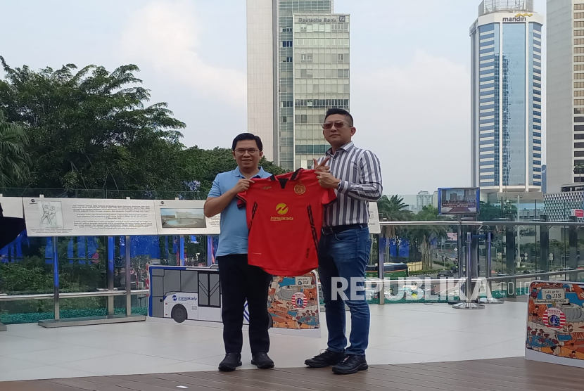 Direktur Utama Transjakarta Welfizon Yuza (kiri) dan Direktur Persija Jakarta Mohamad Prapanca memegang kostum Persija setelah penandatanganan MoU di Halte Astra Bundaran HI, Jakarta Pusat, Selasa (15/7/2025). Dalam kerja sama itu, nantinya akan ada 30 unit bus Transjakarta yang didesain dengan logo Persija. 
