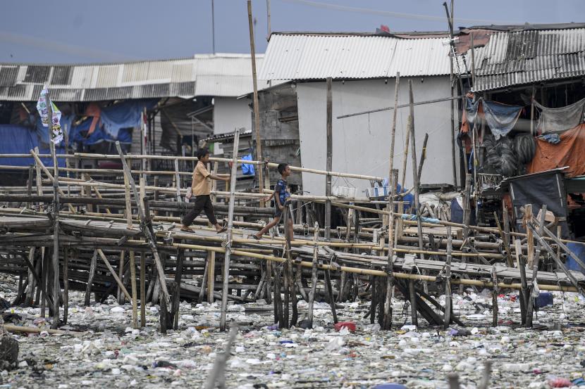 Dua anak berjalan meniti jembatan bambu yang penuh sampah di sekitarnya, di kawasan Kalibaru, Cilincing, Jakarta Utara, Rabu (8/6/2022). Pemprov DKI akan melibatkan seluruh RW di Jakarta ke dalam program sadar sampah.