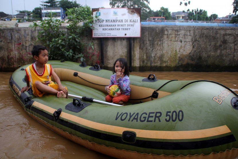 Dua anak bermain genangan air banjir dengan menaiki perahu karet di kelurahan Bukit Duri, Jakarta, Selasa (8/3).