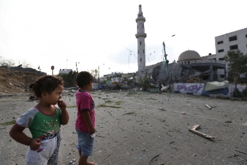 Dua anak di Jalur Gaza melihat bangunan di sekitarnya hancur diserang militer Israel.