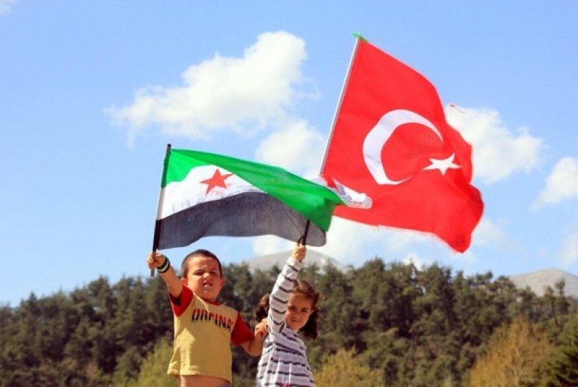 Dua anak kecil melambaikan bendera Turki dan Suriah dekat perbatasan dua negara