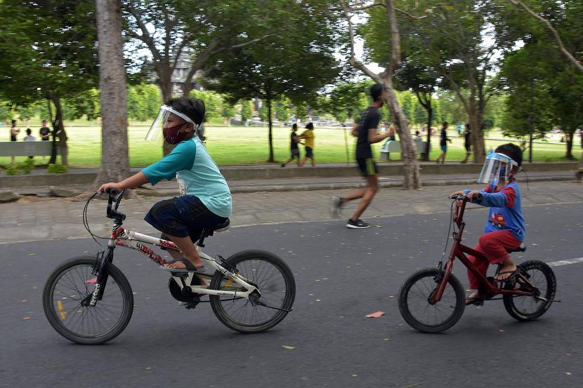 Dua anak memakai pelindung wajah saat bermain sepeda.
