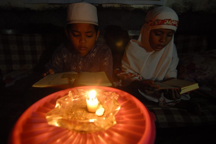 Dua anak membaca Alquran menggunakan penerangan lilin