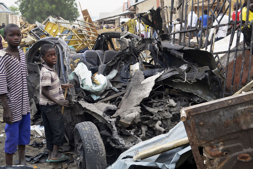 Dua bocah Nigeria berdiri dekat bangkai mobil bekas serangan bom yang diduga dilakukan oleh Boko Haram.