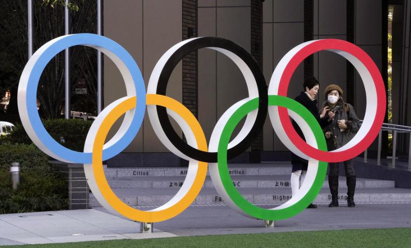 Dua orang berdiri di belakang logo Olimpiade di Tokyo, Jepang. Virus corona telah mengancam kemungkinan terselenggaranya Olimpiade 2020 di Tokyo pada 2021.