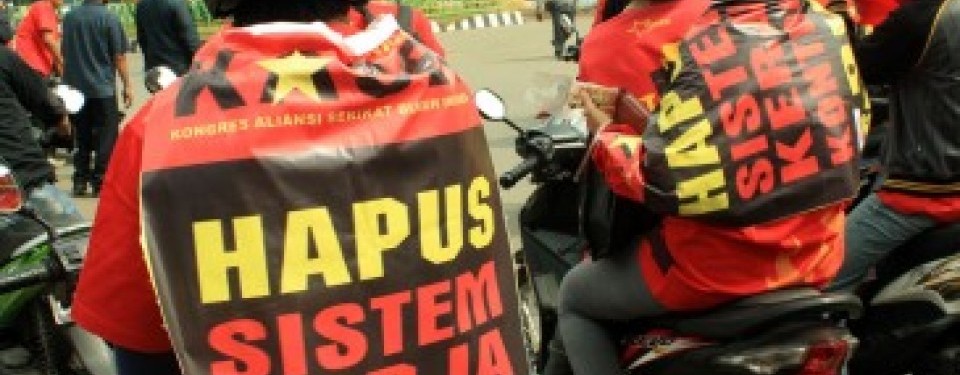 Dua orang buruh yang tergabung dalam Federasi Serikat Pekerja Karawang menempelkan poster berisi tuntutan menghapus sistem kerja kontrak pada kaosnya, saat unjuk rasa memperingati Hari Buruh Internasional, di Bundaran Mega M, Karawang, Jabar, Minggu (1/5).