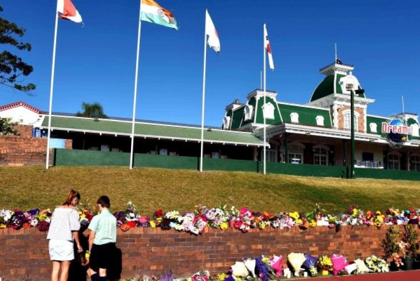 Dua orang menaruh rangkaian bunga di depan Dreamworld, Gold Coast, Queensland (26/10).