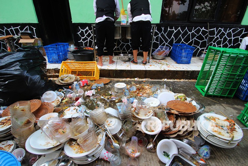 Dua orang petugas catering membersihkan sampah sisa makanan acara resepsi