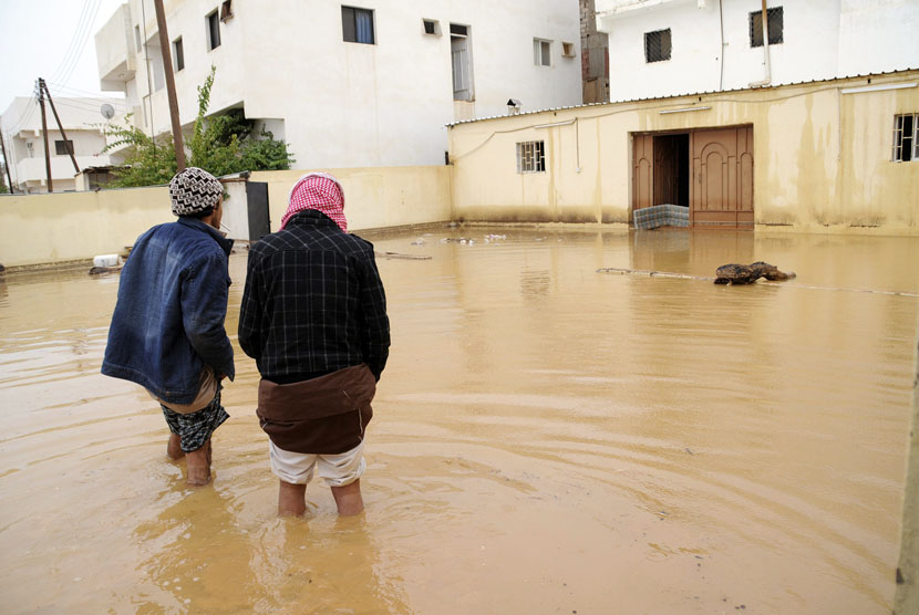  Dua orang pria berjalan di dekat rumah mereka yang terendam banjir setelah hujan lebat di Tabuk, Arab Saudi, Senin (28/1).   (Reuters/Mohamed Alhwaity)