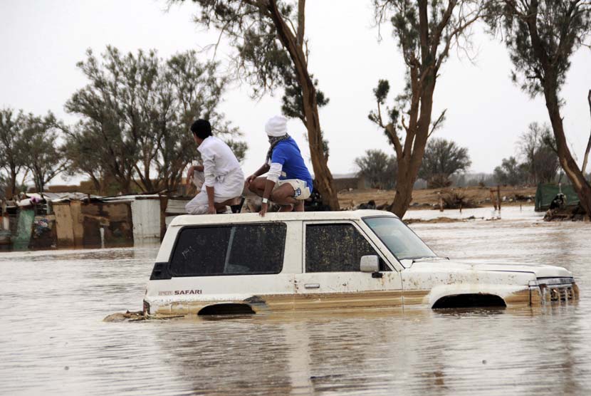   Dua orang pria duduk diatas mobil mereka yang terendam banjir setelah hujan lebat di Tabuk, Arab Saudi, Senin (28/1).   (Reuters/Mohamed Alhwaity)