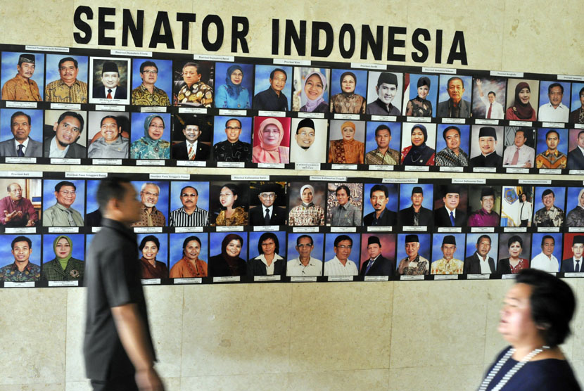 Dua orang pria melintas di depan deretan foto anggota Dewan Perwakilan Daerah (DPD) di Kompleks Parlemen, Senayan, Jakarta.