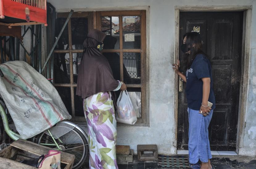 Dua orang warga memberikan bantuan sembako kepada kerabatnya yang sedang menjalani isolasi mandiri di Kampung Sambongpari, Kota Tasikmalaya, Jawa Barat, Senin (21/6/2021). Warga RW 04 di Kampung Sambongpari tersebut melakukan karantina wilayah mandiri menyusul 15 warganya terkonfirmasi positif COVID-19, satu di antaranya meninggal dunia usai berwisata ke Pangandaran. 