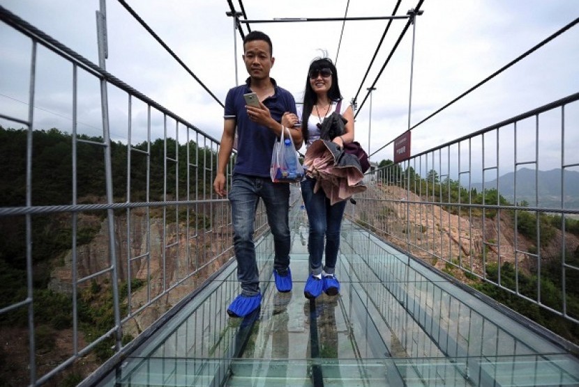 Dua orang wisatawan tengah berjalan di jembatan gantung yang terbuat dari kaca di Cina