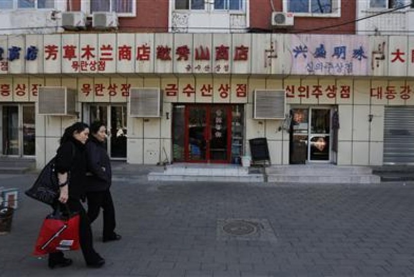 Dua perempuan berjalan di toko dengan tulisan bahasa Korea di dekat Kedutaan Besar Korea Utara di Beijing