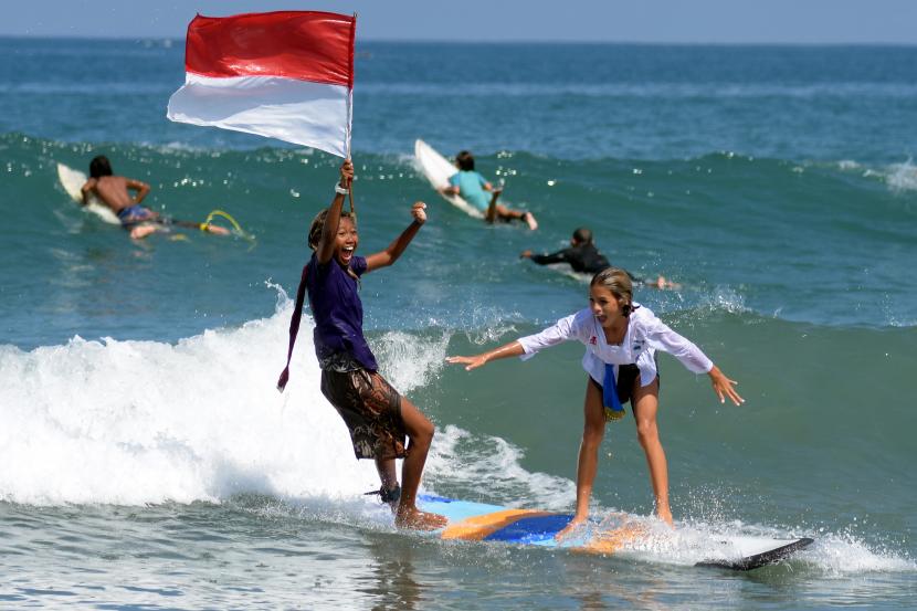 Dua peselancar wanita mengenakan pakaian kebaya sambil mengibarkan bendera Merah Putih saat beratraksi di Pantai Kuta, Badung, Bali, Sabtu (16/4/2022). Atraksi selancar untuk menyambut Hari Kartini itu sekaligus sebagai daya tarik wisata guna membangkitkan pariwisata Bali yang terdampak pandemi COVID-19. 