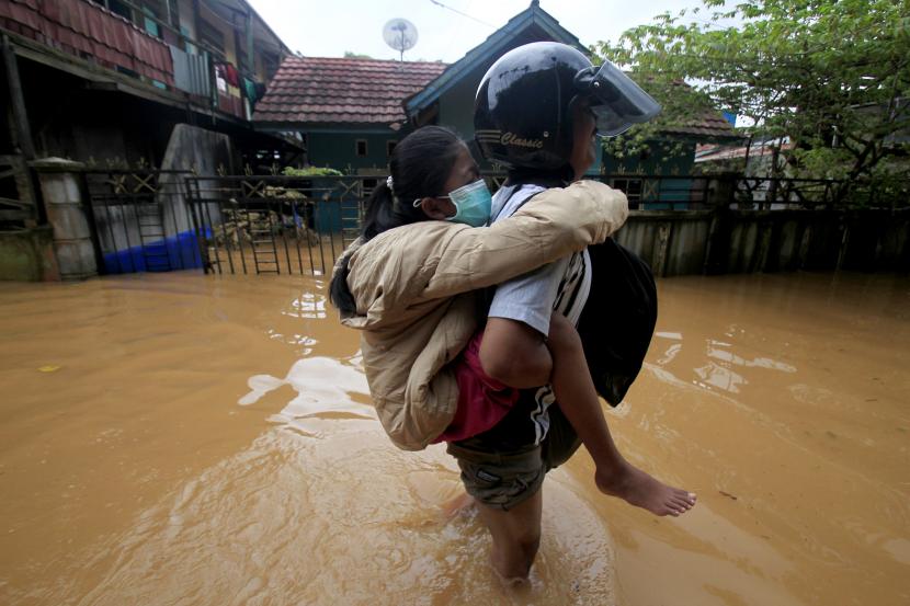 Dua warga melintasi daerah yang masih terendam banjir di Perumahan Organda, Distri Heram, Kota Jayapura, Papua, Ahad (9/1/2022). Sekitar tujuh ribu warga terdampak banjir dan longsor yang terjadi pada Jumat (7/1/2022).