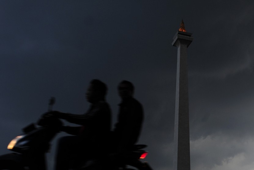 Dua warga mengendarai sepeda motor melintasi Monas yang diselimuti awan hitam di Kawasan Monas, Jakarta, Senin (30/11). 