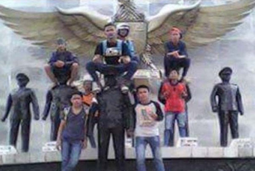 Foto sejumlah pemuda yang duduk diatas patung pahlawan