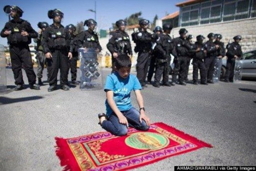 Foto seorang bocah laki-laki yang sedang shalat membelakangi barisan tentara Israel