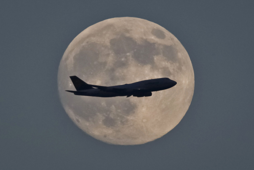 Pesawat terbang melintas di udara dengan latar bulan purnama. (Ilustrasi)