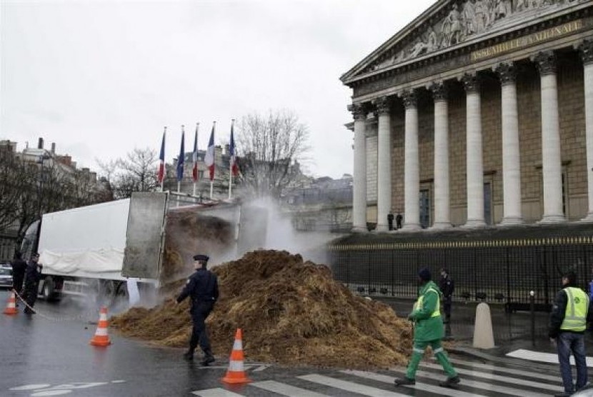 French police and municipal workers walk near a large pile of manure sitting in front of the National Assembly in Paris January 16, 2014.