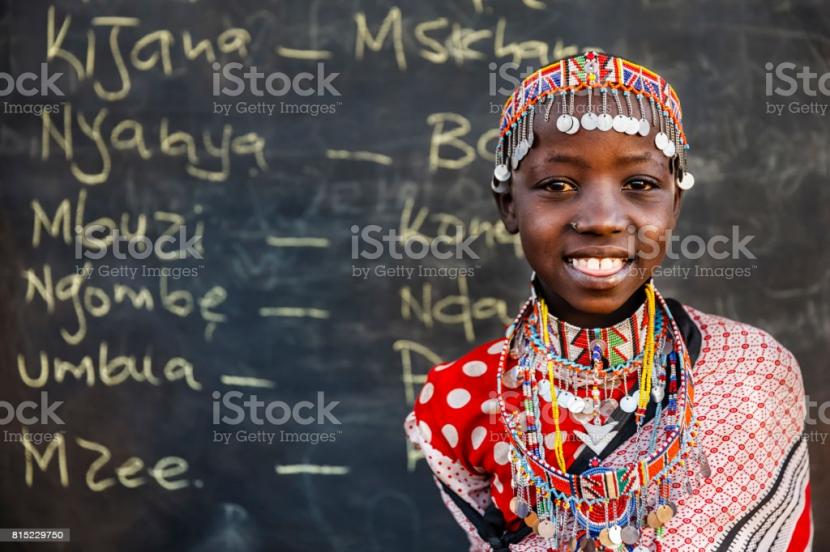 Gadis Swahii berdiri di depan sejumllah tulisan kosakata Swahili