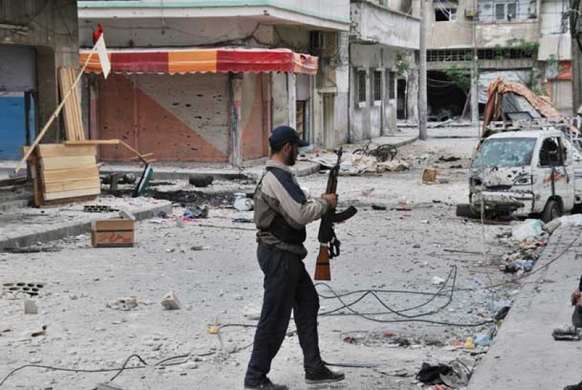  Gerilyawan penentang rezim pemerintah Suriah berjalan melewati kawasan pertokoan yang hancur di kota Homs, Suriah. 