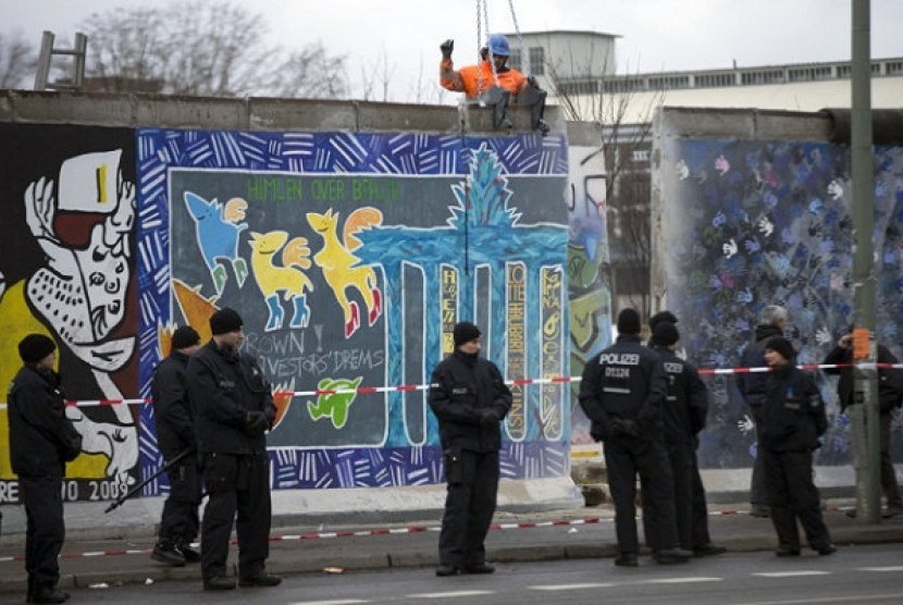 German police officers protect a part of the former Berlin Wall in Berlin, Germany, Friday, March 1, 2013. Berliners are protesting as a construction company removes a section of a historic stretch of the Berlin Wall known as the East Side Gallery to provi