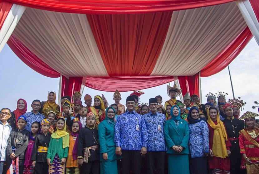 Gubernur DKI Jakarta Anies Baswedan (tengah) dan istri, Fery Farhati (kedelapan kiri) serta Wakil Gubernur DKI Jakarta Sandiaga Uno (ketujuh kanan) dan istri, Nur Asia (keenam kanan) berfoto bersama anak-anak dengan baju daerah saat hadir dalam peringatan Hari Sumpah Pemuda ke-89 di Lapangan IRTI Monas, Jakarta, Senin (30/10). 