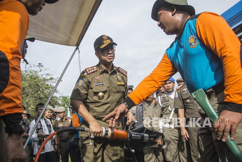 Gubernur DKI Jakarta Anies Baswedan (tengah) mendengan penjelasan anggota Satpol PP tentang fungsi alat mesin potong yang dipamerkan dalam Apel Besar Rotasi Satuan Polisi Pamong Praja (Satpol PP) DKI Jakarta di Monumen Nasional (Monas) , Jakarta, Jumat (29/12). 