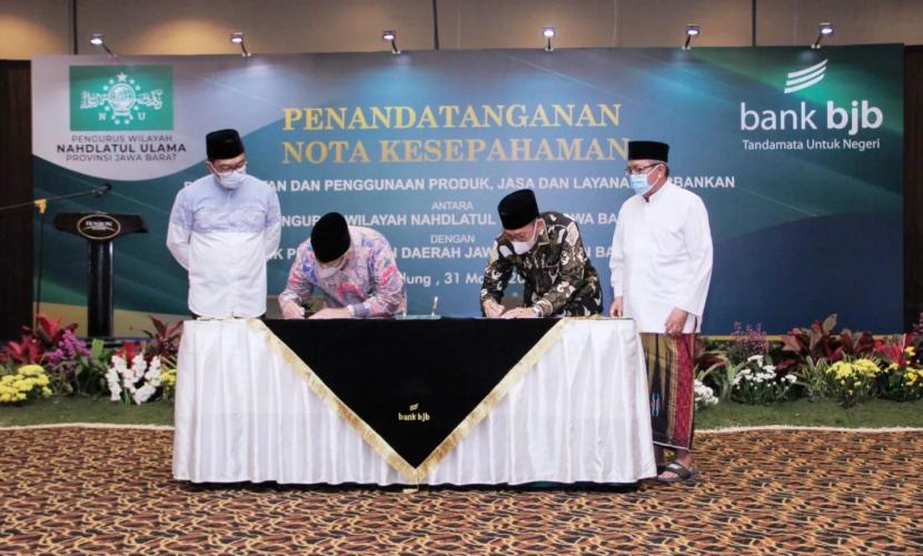 Gubernur Jabar Ridwan Kamil (kiri) menyaksikan Dirut Bank BJB Yuddy Renaldi (kedua kiri) dan Ketua PWNU Jabar KH Juhadi Muhammad yang tengah menandatangani MoU terkait program perekonomian umat di Hotel Horison Bandung, Kamis (31/3). 