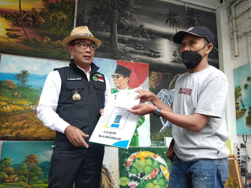 Gubernur Jawa Barat Ridwan Kamil menyerahkan uang hasil penjualan lukisan kaligrafi yang dijual melalui Non-Fungible Token (NTF) ke Pelukis Jalan Braga, Solihin,di Jalan Braga, Kota Bandung