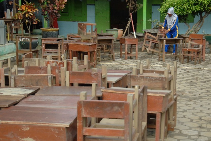 Guru mengeluarkan meja dan kursi ketika membersihkan ruang kelas yang tergenang banjir di SDN Rongtengah 1, Sampang, Jatim, Selasa (1/3).