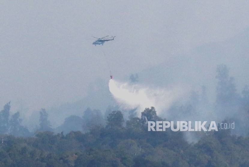 Helikopter melakukan water bombing di atas hutan yang terbakar, ilustrasi