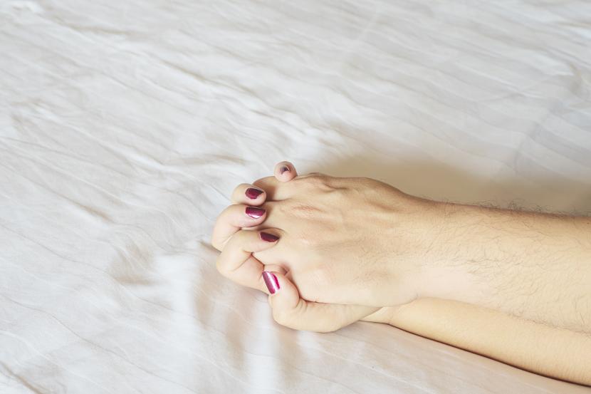 Pria dan wanita saling menggenggam tangan di atas kasur (ilustrasi). Berhubungan seks di luar pernikahan banyak bahayanya.