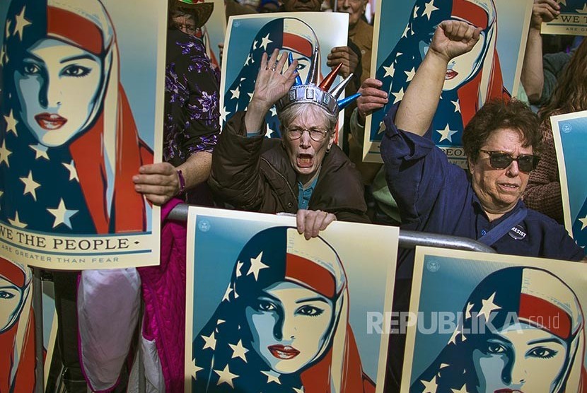 I am a Muslim Too: Pengunjukrasa membawa poster bergambar wanita berhijab bendera Amerika di sela unjuk rasa menolak kebijakan Anti Imigran Trump di Lapang Times Square New York, AS, (19/2) waktu setempat. 