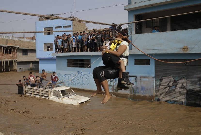 Ibu dan anaknya ditarik menggunakan tali untuk memindahkan dari tempat tempat banjir di Lima, Peru, (17/3).