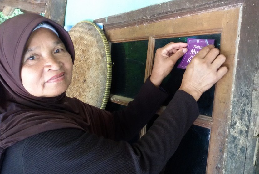 Ibu Keni sedang menempelkan stiker Amartha di warung nasi uduk miliknya