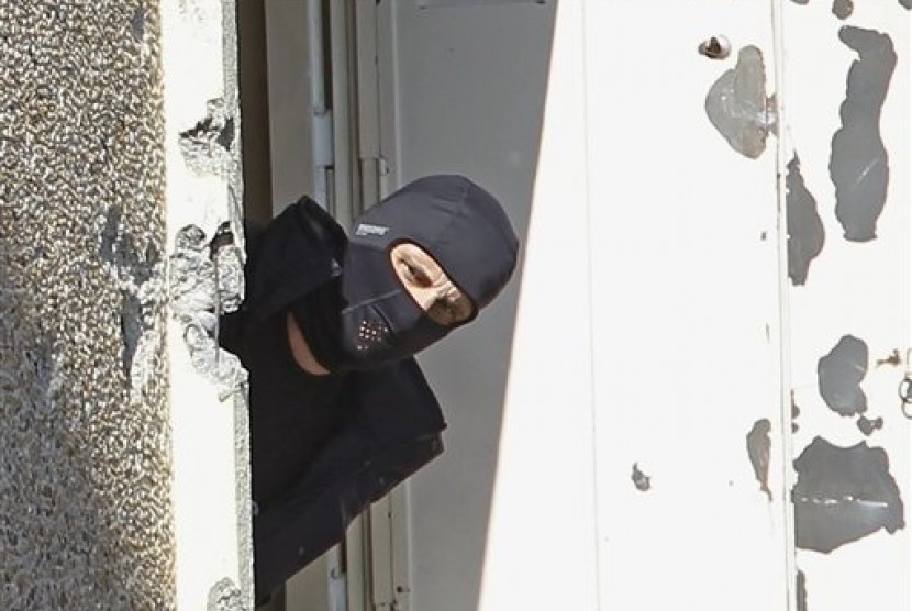 In this March 23, 2014 file photo, a masked police officer searches for clues at terrorist Mohamed Merah's apartment building in Toulouse, southern France. 