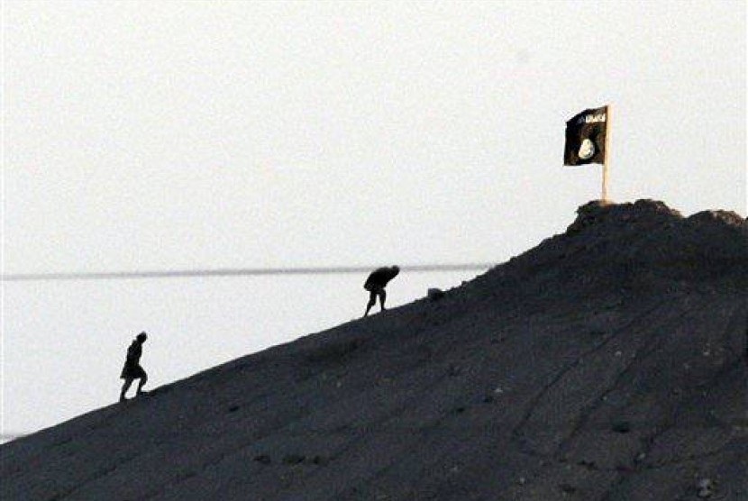 In this Oct. 6, 2014 file photo, shot with an extreme telephoto lens from the outskirts of Suruc at the Turkey-Syria border, militants with the Islamic State group are seen after placing their group's flag on a hilltop at the eastern side of Kobani, Syria.