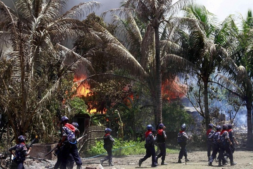 In this photo taken on June 12, 2012, Myanmar policemen walk towards burning buildings in Sittwe, capital of Rakhine state in western Myanmar. Communal violence is grinding on in western Myanmar six weeks after the government declared a state of emergency 