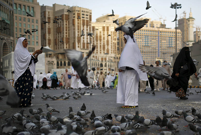 Jamaah haji berjalan melintasi kawanan  burung merpati di kota suci Makkah.