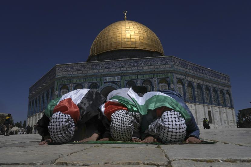 Jamaah Muslim yang dibungkus dengan bendera Palestina berdoa selama bulan suci Ramadhan di depan kuil Dome of the Rock di kompleks Masjid Al Aqsa di Kota Tua Yerusalem, Jumat, 15 April 2022. Liga Arab: Israel tak Berhak Putuskan Siapa yang Bisa Masuki Masjid Al Aqsa