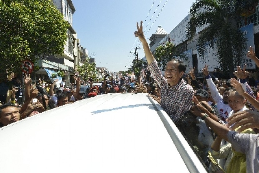  Jokowi mengacungkan salam dua jari kepada warga ketika berkunjung ke kawasan Pasar Kota, Gresik, Jawa Timur, Ahad (29/6).