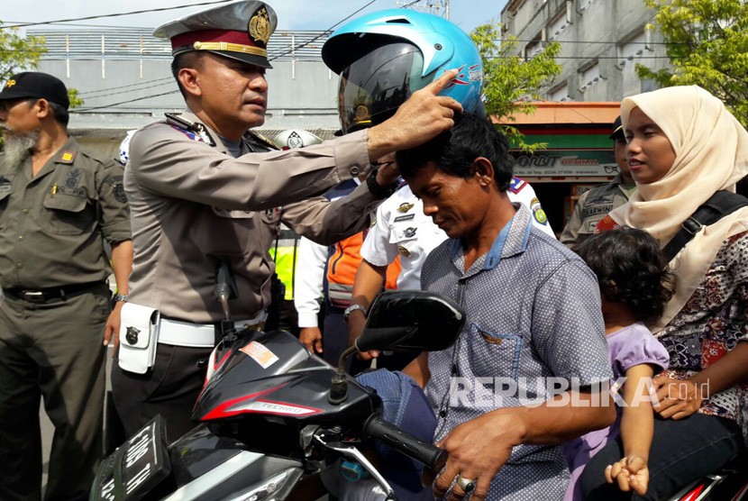 Kanit Regident Polres Indramayu, Iptu Tenda, memasangkan helm kepada seorang pengguna sepeda motor yang diketahui tidak mengenakan helm saat berkendara, Senin (6/3).